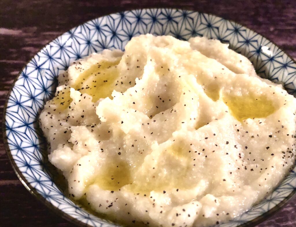 Bowl of mashed cauliflower with melted butter and black pepper