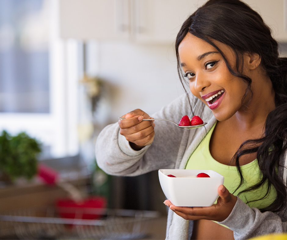 young woman eating berries from a bowl with a smile on her face