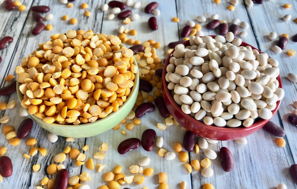 small bowls filled with yellow lentils and white beans, kidney beans scattered about