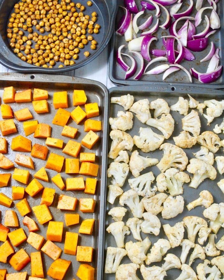 Cauliflower, butternut squash and red onion pieces scattered on baking sheets