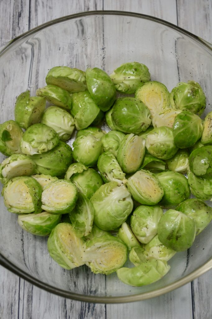 Halved Brussels Sprouts in a bowl tossed with olive oil, salt & pepper