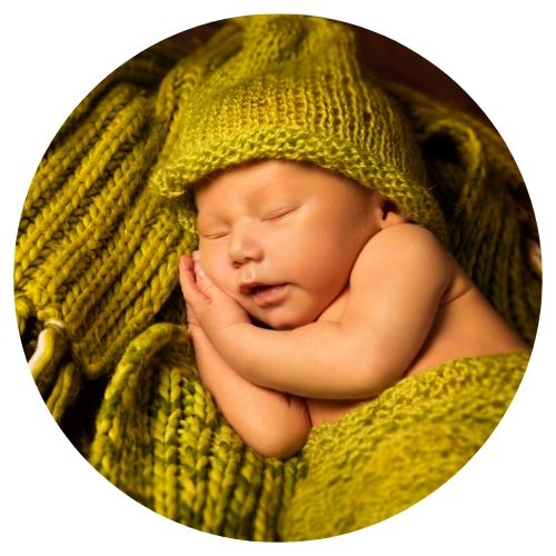 newborn sleeping with hands under his face with greenish yellow crocheted hat and blanket