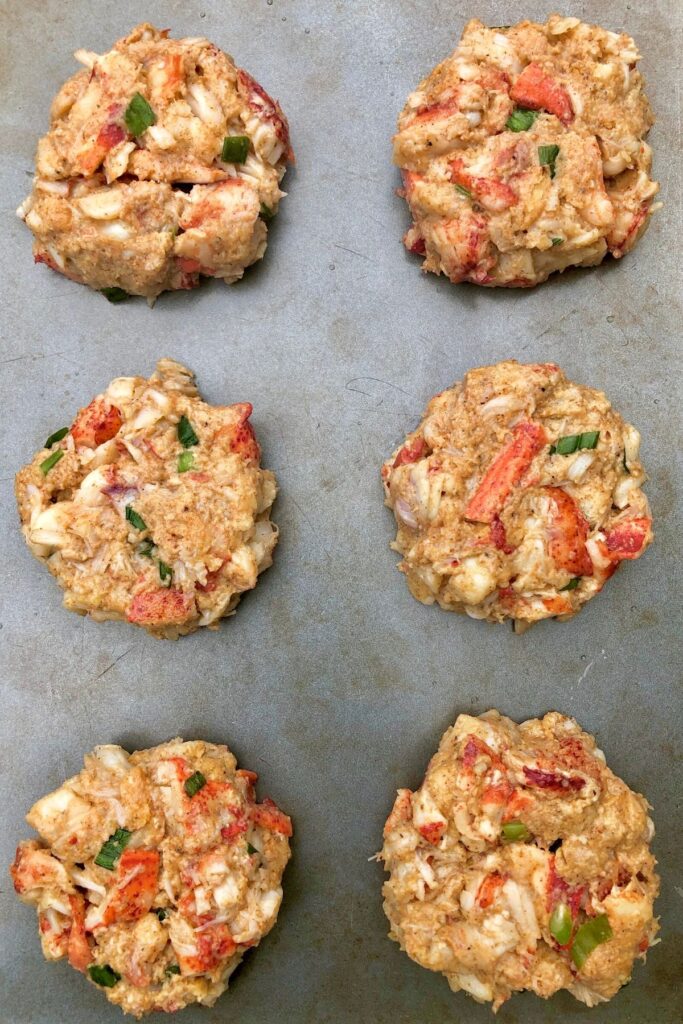 4 raw lobster cakes on a baking sheet