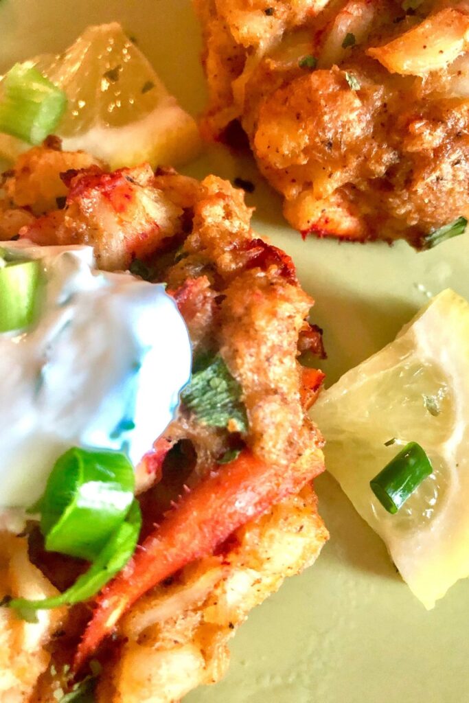 Lobster cake garnished with a dollop of lemon Dill Yogurt Sauce, lemon slice and green onion