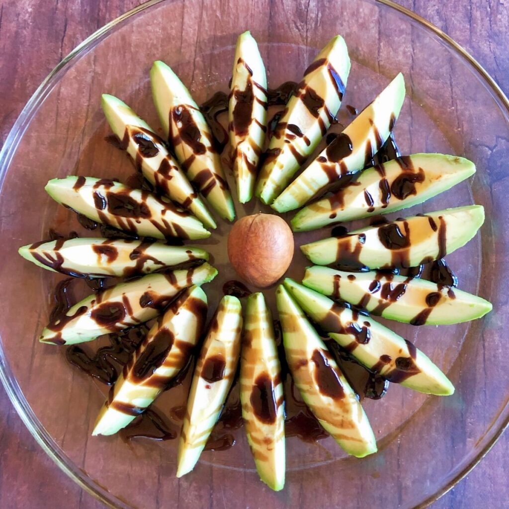 Avocado slices arranged around the pit to resemble a flower and drizzled with balsamic glaze
