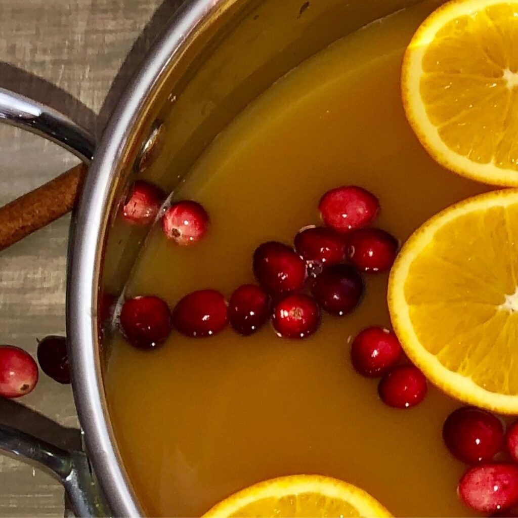 pot of mulled cider with cranberries, sliced oranges, and cinnamon sticks