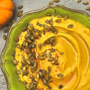 pumpkin hummus in green bowl topped with roasted pepitas