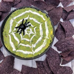 Bowl of guacamole with spider web and spider surrounded by black corn tortilla chips