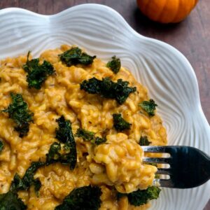 Pumpkin Risotto in white decorative bowl on brown table with small pumpkin to side