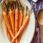 roasted carrots in oval dish on wooden table with wooden spoon to side