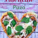 heart shaped pizza with spinach and red onion on wire rack on pink wooden backdrop