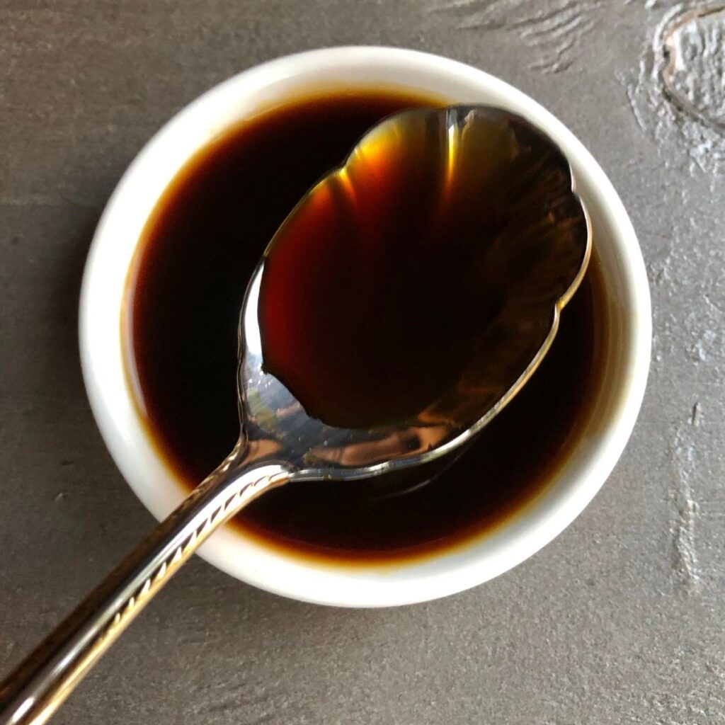 A white dish and spoon of coconut aminos