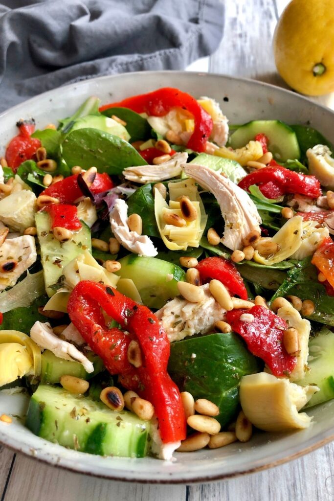 Mediterranean Chicken Salad with greens, chicken, roasted red peppers, artichoke hearts, cucumbers, and toasted pine nuts