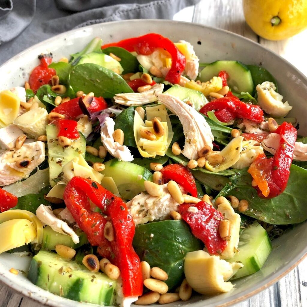 Mediterranean Chicken Salad with greens, chicken, roasted red peppers, artichoke hearts, cucumbers, and toasted pine nuts