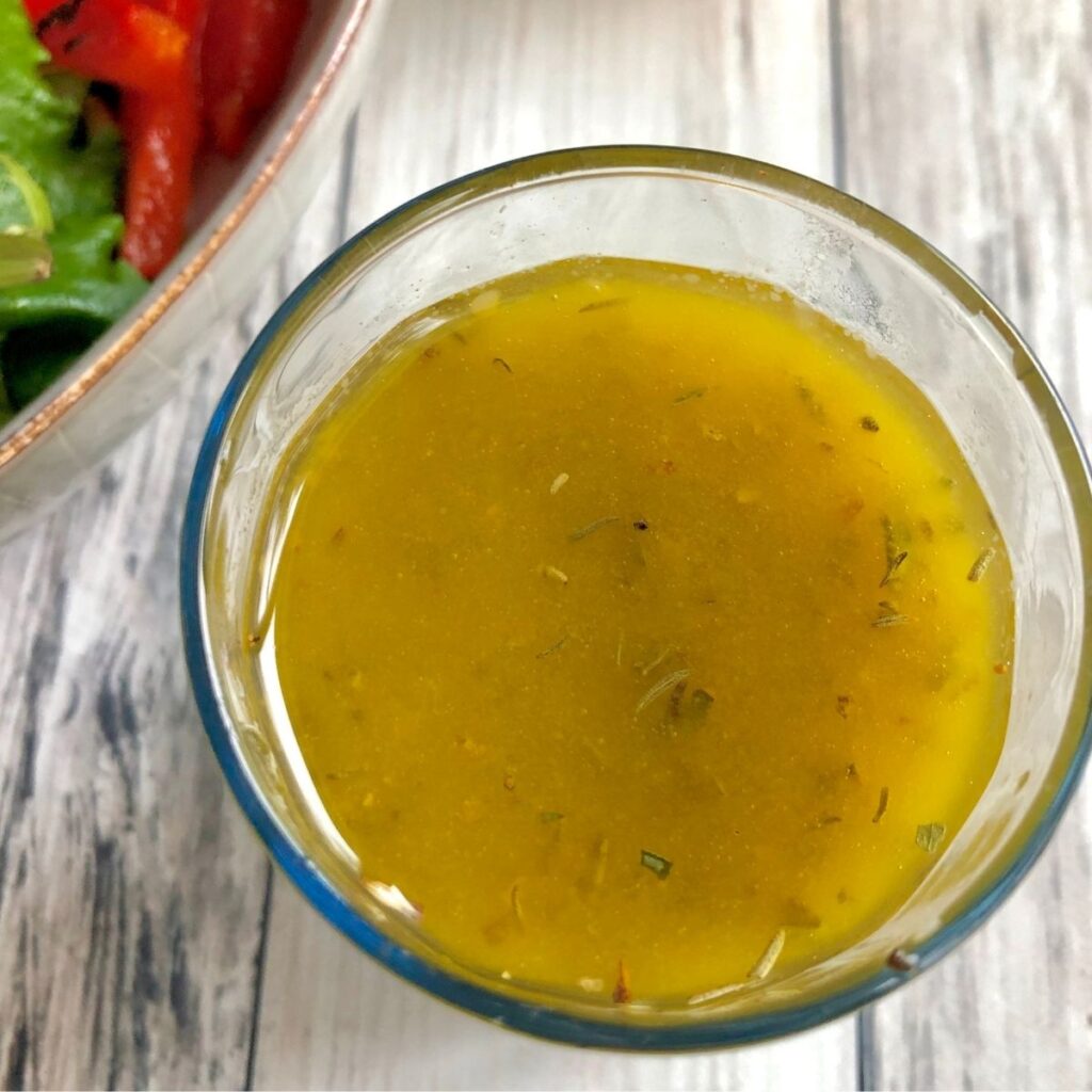 homemade Mediterranean Salad Dressing in a small glass next to a salad