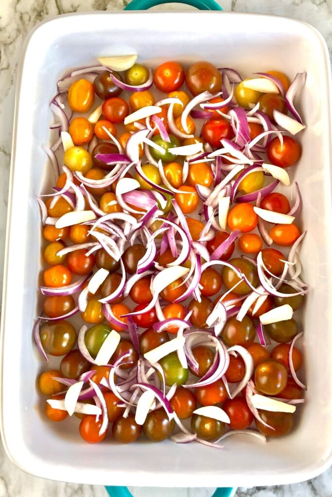 multi-colored cherry tomatoes, sliced red onion, and slivered garlic cloves in a baking dish