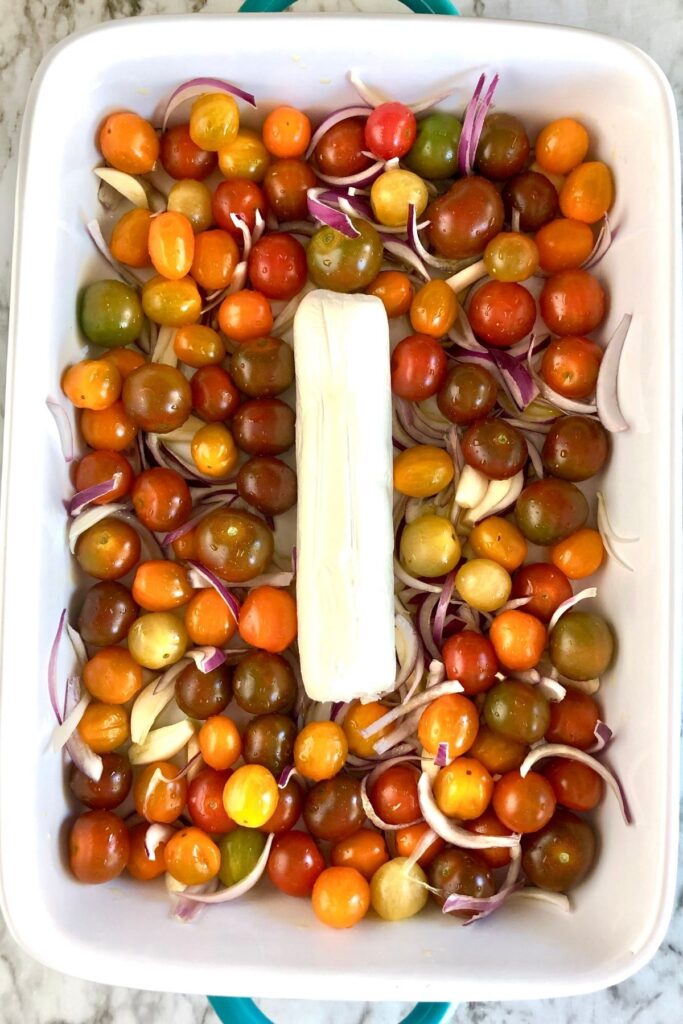 a 9x13 baking dish full of multi-colored cherry tomatoes, red onion slices with a goat cheese log in the center