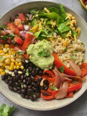 bowl of cilantro lime rice, pico de gallo, lettuce, cheese, corn, black beans, grilled onions & peppers, avocado sauce and garnished with fresh cilantro