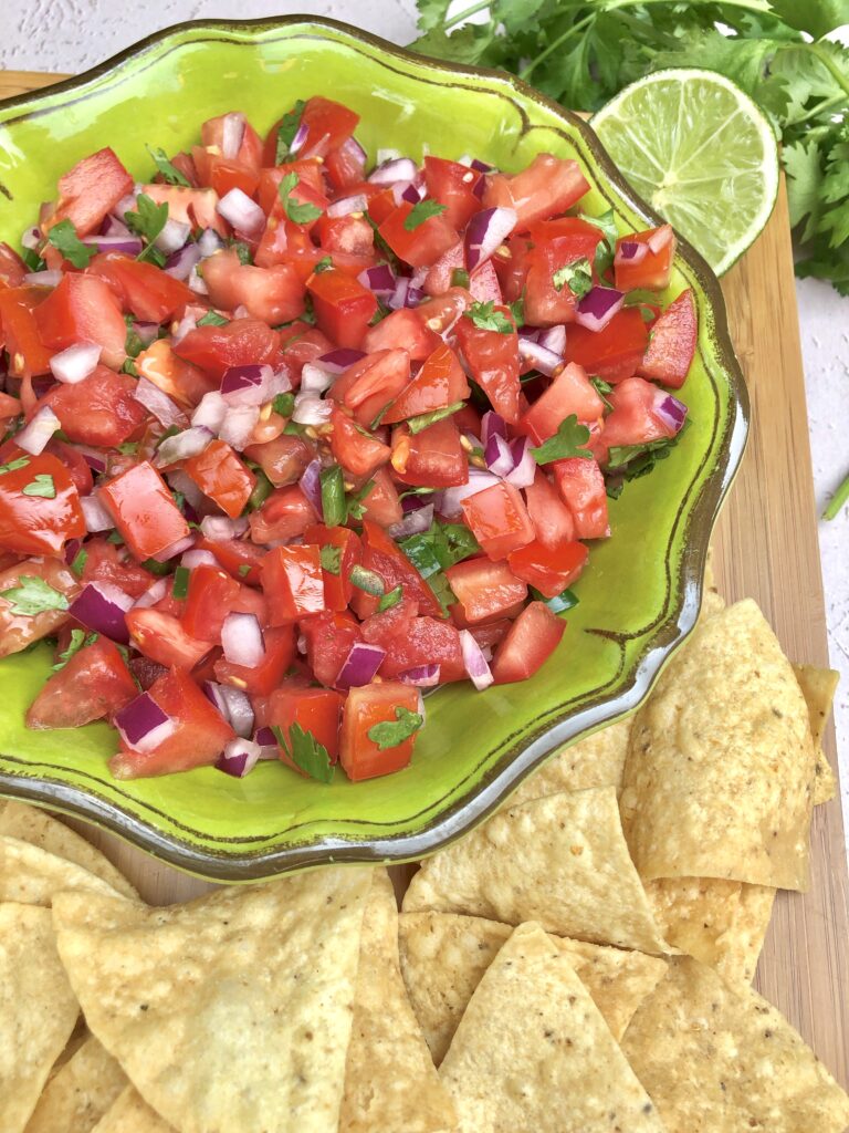 green bowl of pico de gallo on brown platter with tortilla chips