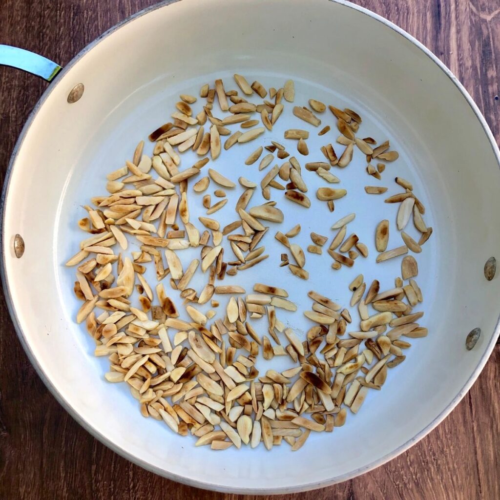 a large white skillet with toasted almond slivers