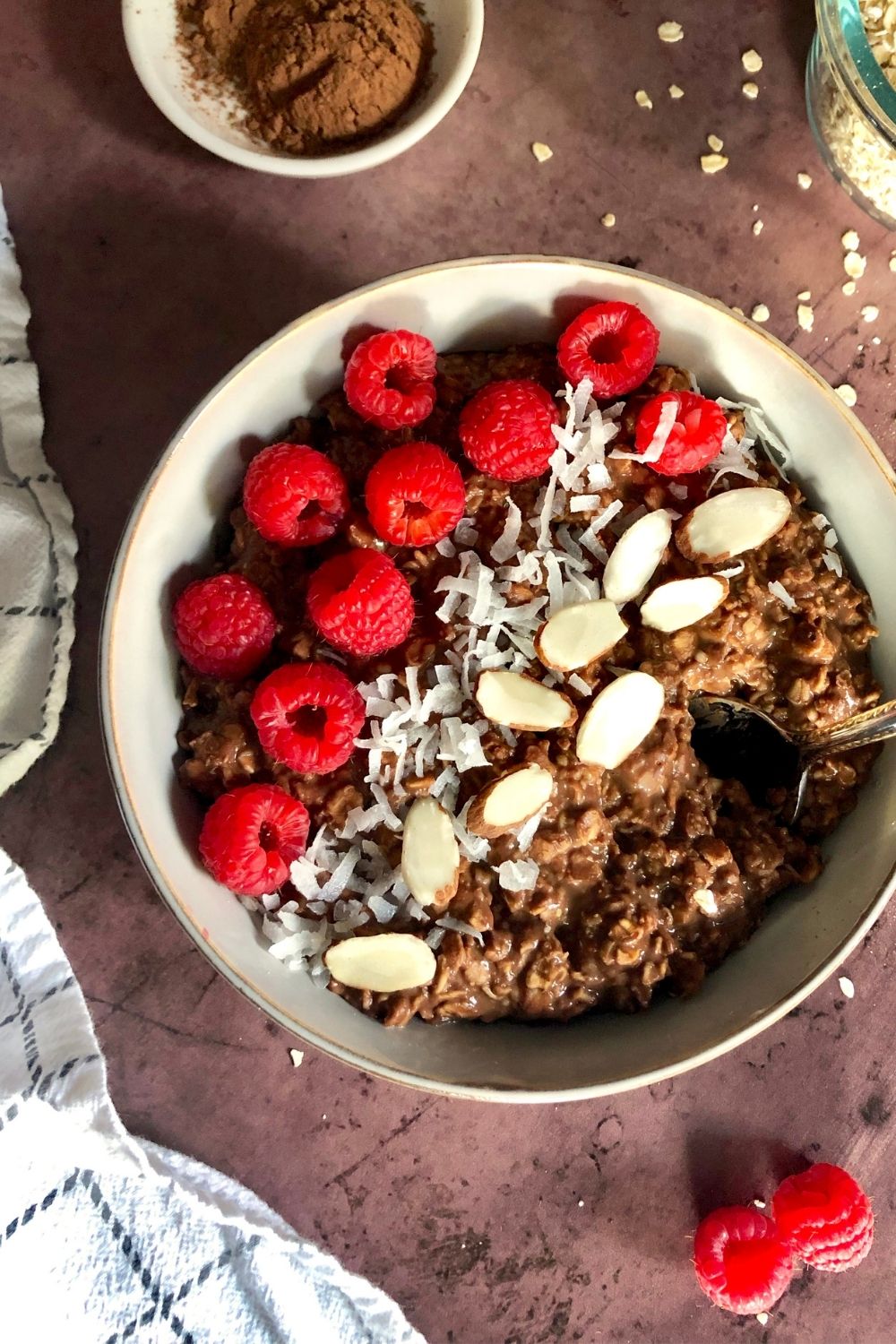 a bowl of chocolate oatmeal garnished with raspberries, coconut flakes, and sliced almonds