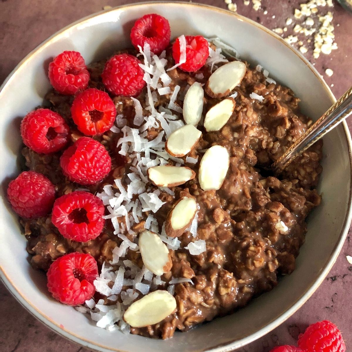 bowl of chocolate oatmeal garnished with raspberries, shredded coconut, and sliced almonds