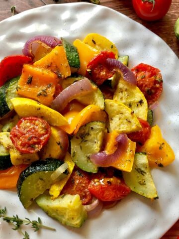 a white plate topped with roasted tomato, zuchhini, red onion, orange bell pepper.