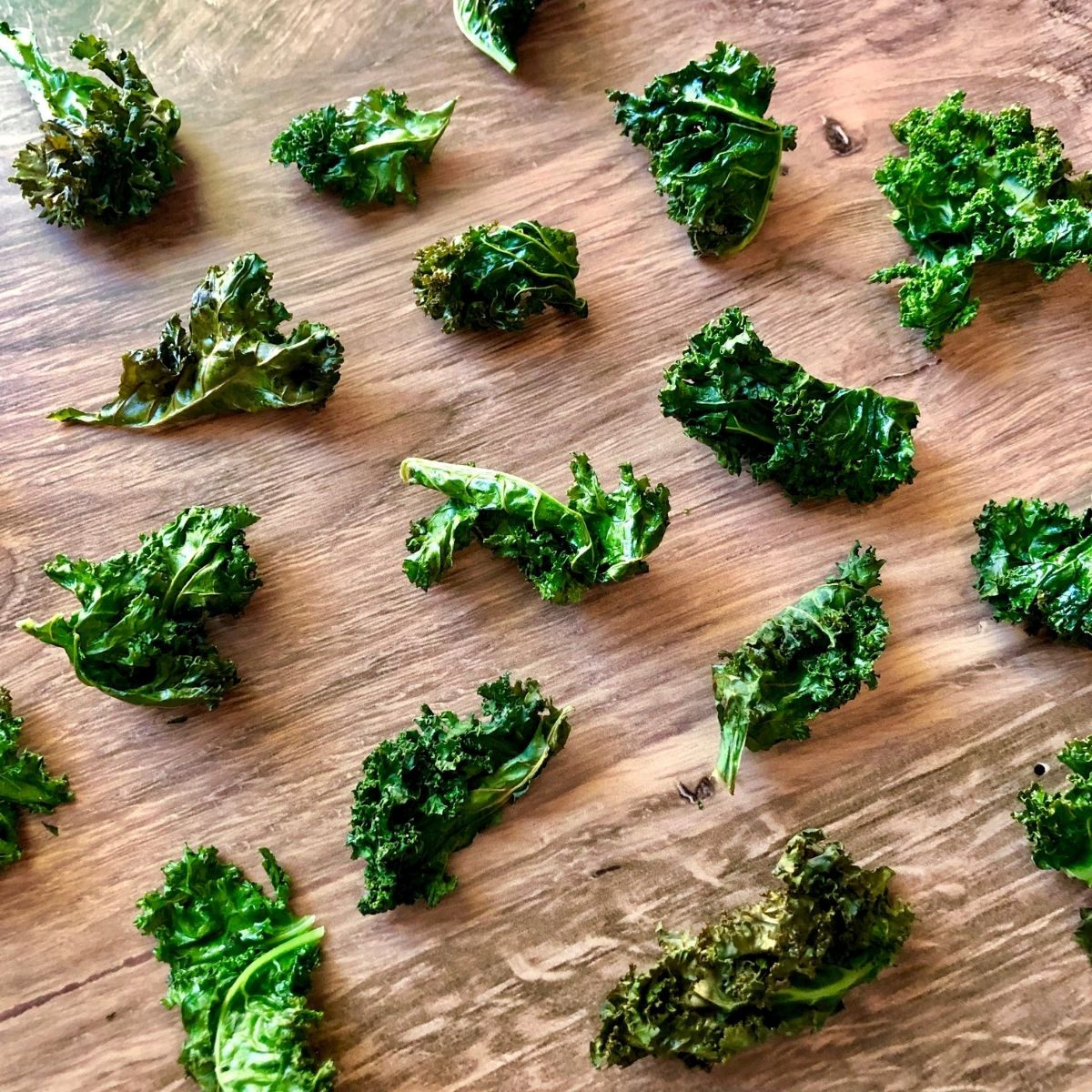scattered cooked kale chips on a wooden table.