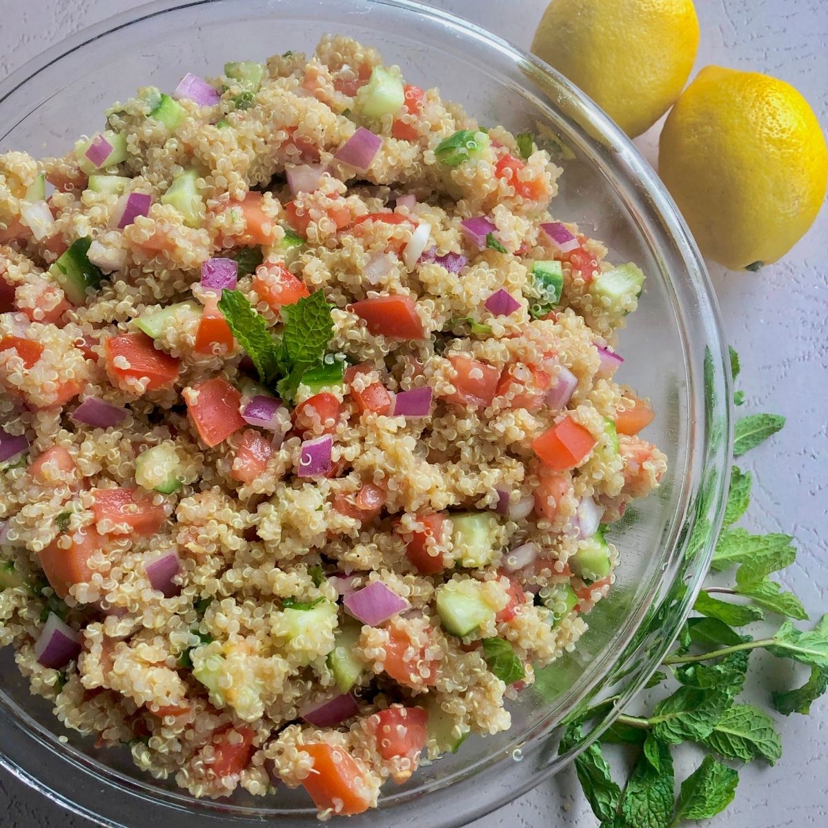 a glass bowl of quinoa salad with lemons and fresh mint off to side