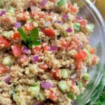 a glass bowl of quinoa salad garnished with fresh mint leaves