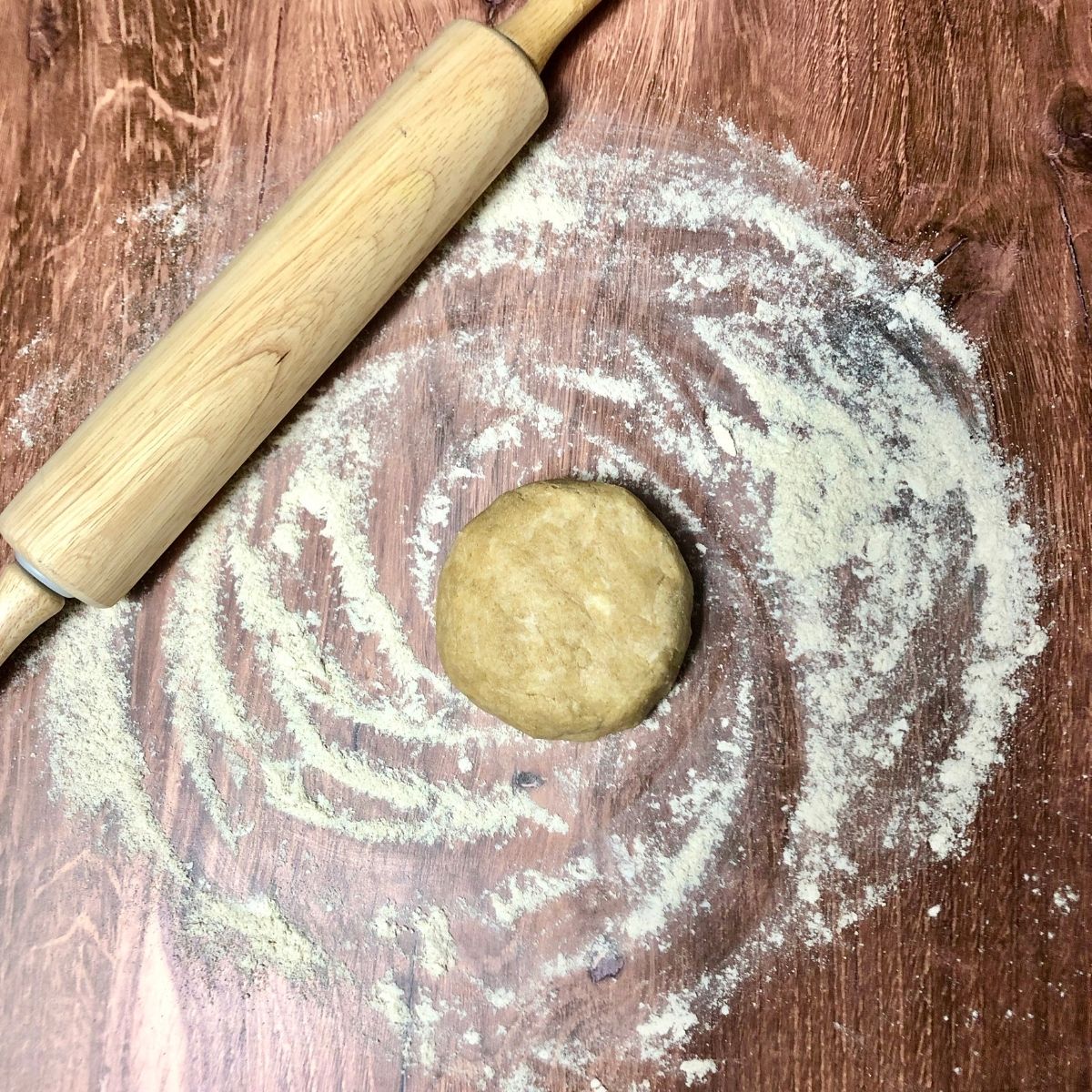 a dough ball on floured wooden surface with rolling pin to side