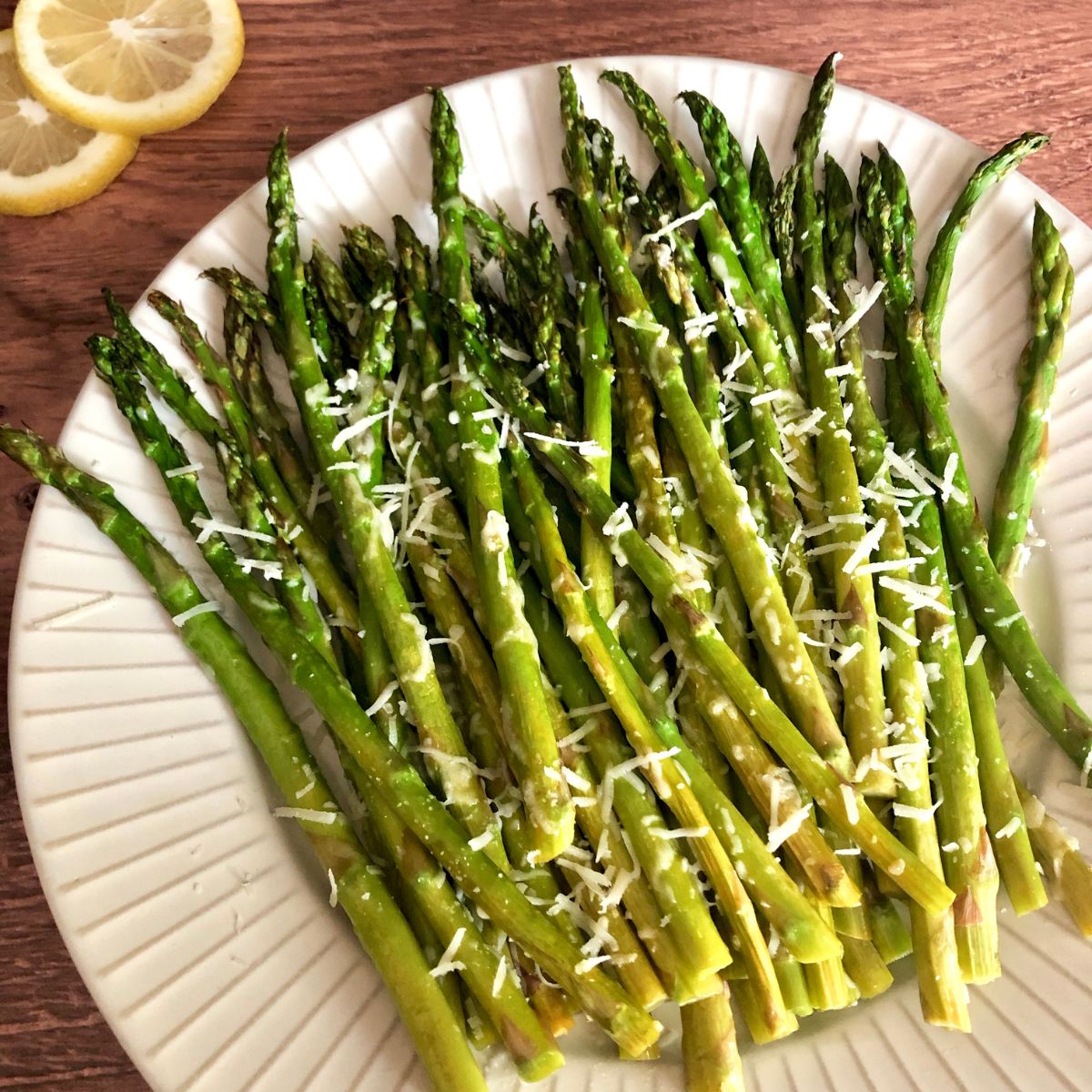 cooked asparagus spears on white plate garnished with graded parmesan with lemon slices to side