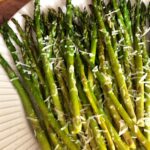 cooked asparagus spears on a white plate with graded parm cheese on top