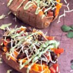two sweet potatoes stuffed with taco ingredients: black beans, salsa, cheese, and avocado sauce