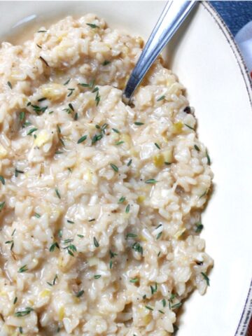 Cheese risotto in an oval white dish with spoon and garnished with fresh thyme