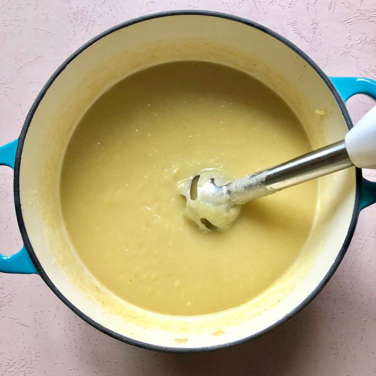 a bowl of potato soup in a light blue dutch oven with an immersion blender in it.