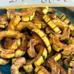 Roasted delicata squash half moons on a teal dish.