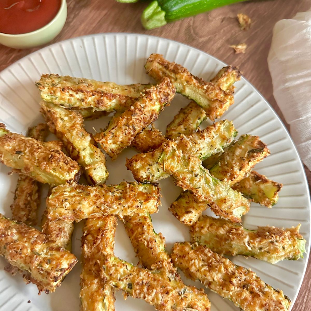 a plate of zucchini fries with a small dish of ketchup off to the side.