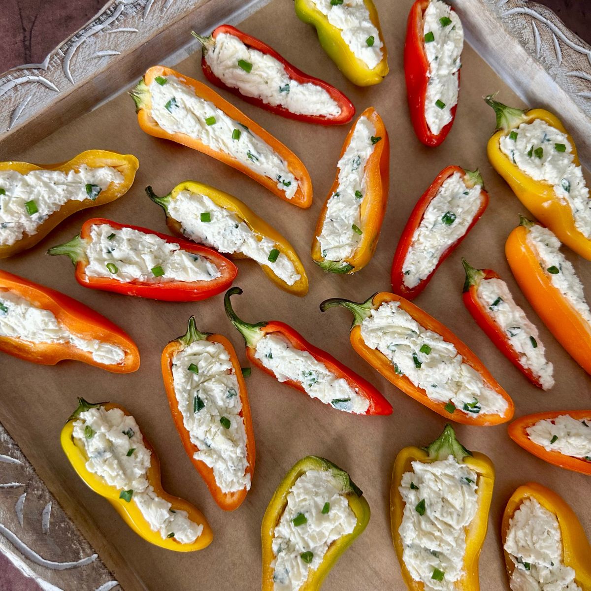 cold cream cheese stuffed mini peppers on a decorative wooden tray.