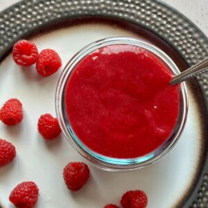 a small dish of raspberry puree with scattered fresh raspberries to side.