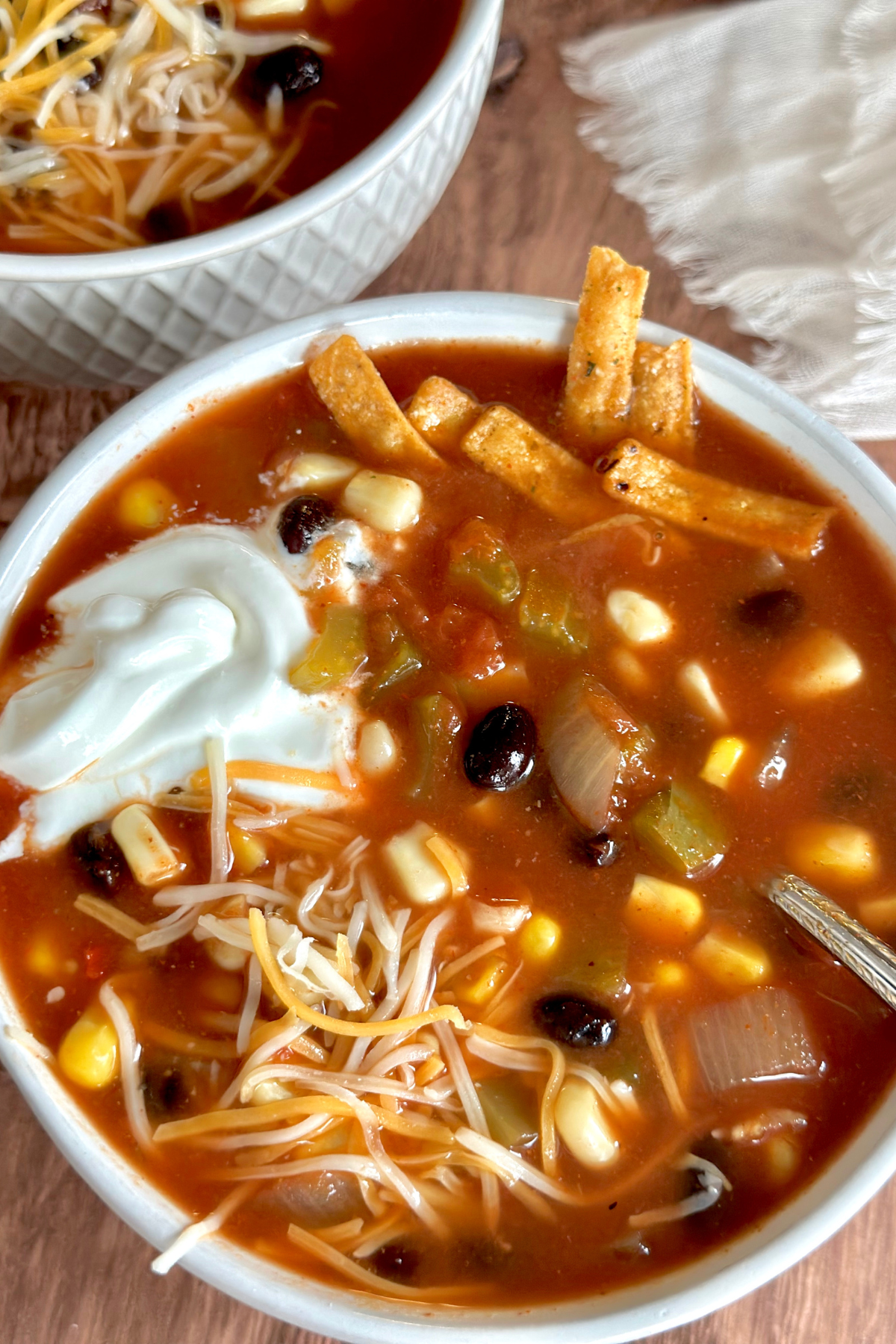 A bowl of Southwestern soup garnished with sour cream, cheese, and tortilla chips.