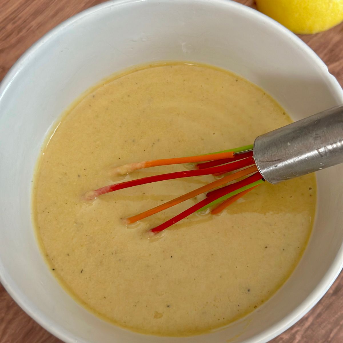 tahini sauce in a small white bowl with red whisk.