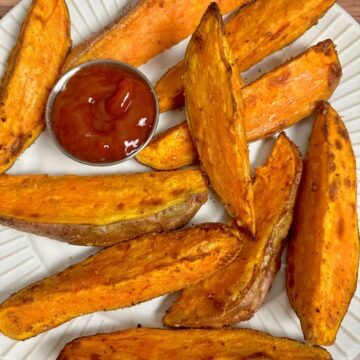 Sweet Potato Wedges on a white plate with condiment cup of ketchup.