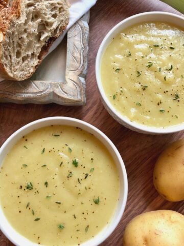 2 bowls of leek potato soup garnished with fresh thyme with crusty bread off to side.