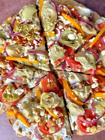 Round pizza topped with tomato, red onion, orange pepper, artichokes and cheese.