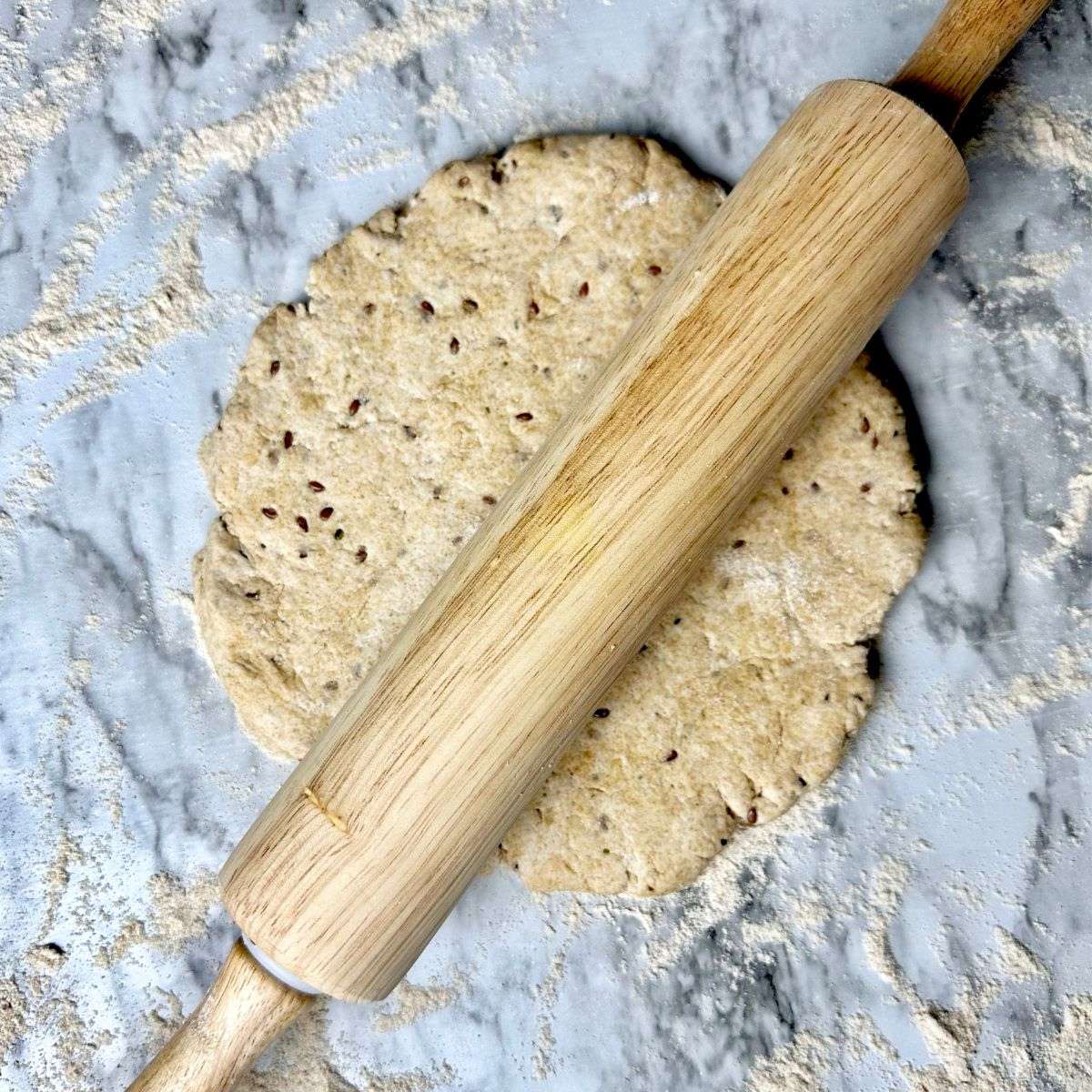 a rolling pin on top of a circular pizza dough.