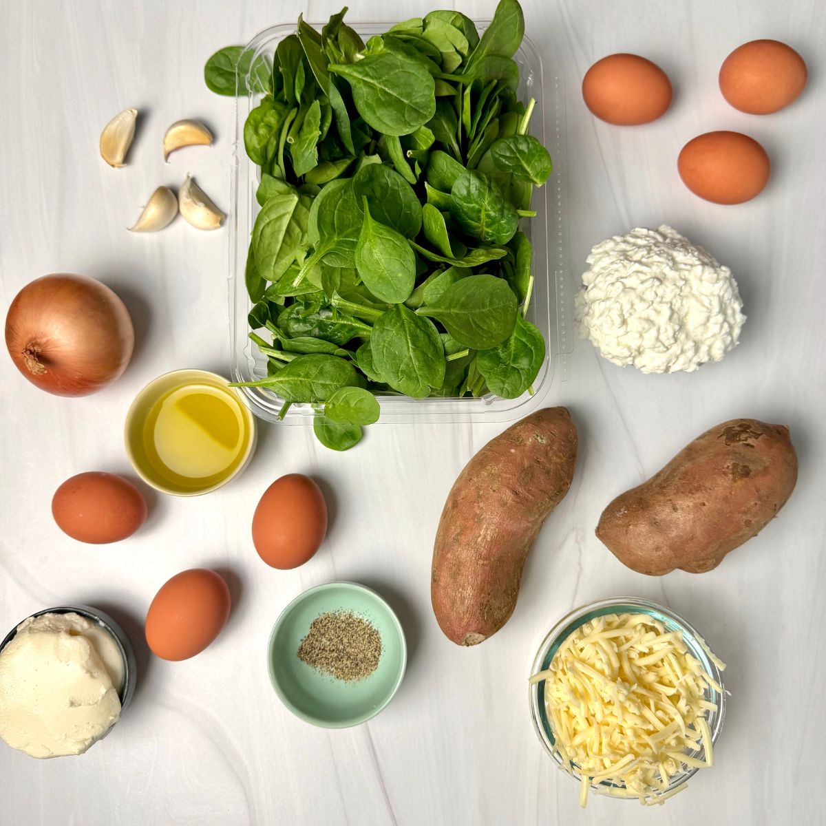 Fresh spinach leaves, 4 cloves of garlic, 6 eggs, 2 sweet potatoes, an onion, black pepper, and bowls of cottage cheese, cheddar cheese, and ricotta cheese.
