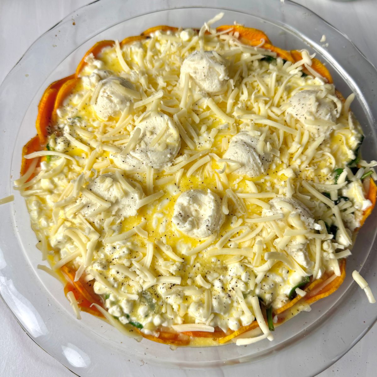Uncooked Quiche with sprinkled cheese and dollops of ricotta cheese on top.